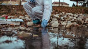 A scientist in protective clothing takes a sample of water for monitoring